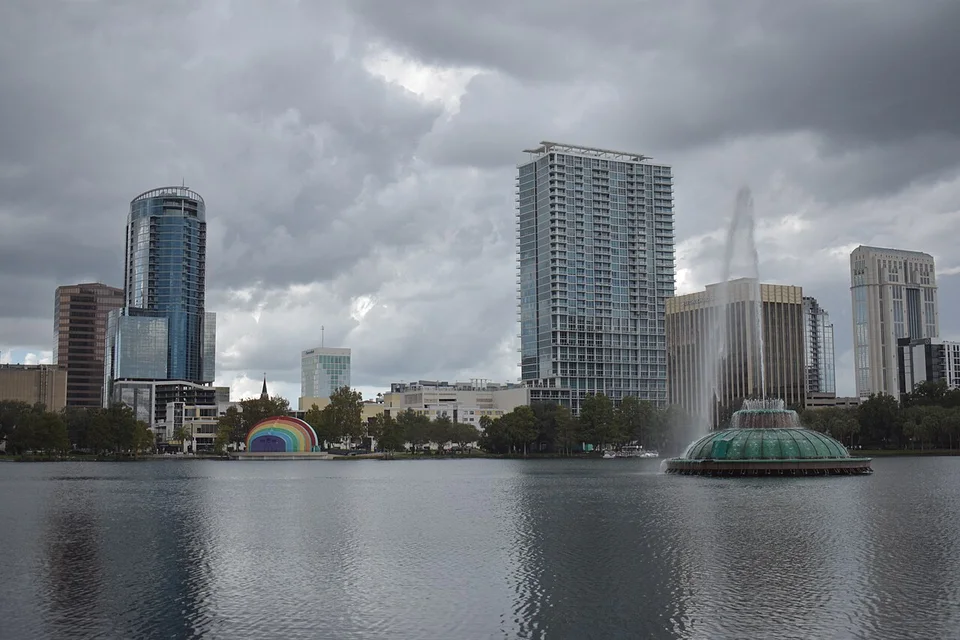 Lake Eola fountain, lakeside amphitheater and downtown Orlando skyline beneath clouds. City-context photograph taken in October 2024. It does not show a theme park or a Christmas event.