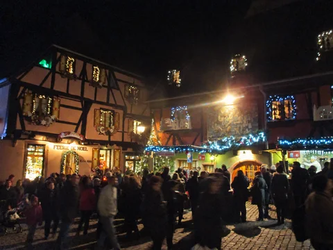 KI-generierte repräsentative Illustration. Fotovorlage: Fachwerkfassaden, Weihnachtsbeleuchtung und Besucher bei Nacht in Riquewihr. Archivaufnahme aus der Weihnachtszeit 2014; sie zeigt eine frühere Szene, nicht die Gestaltung von 2026.