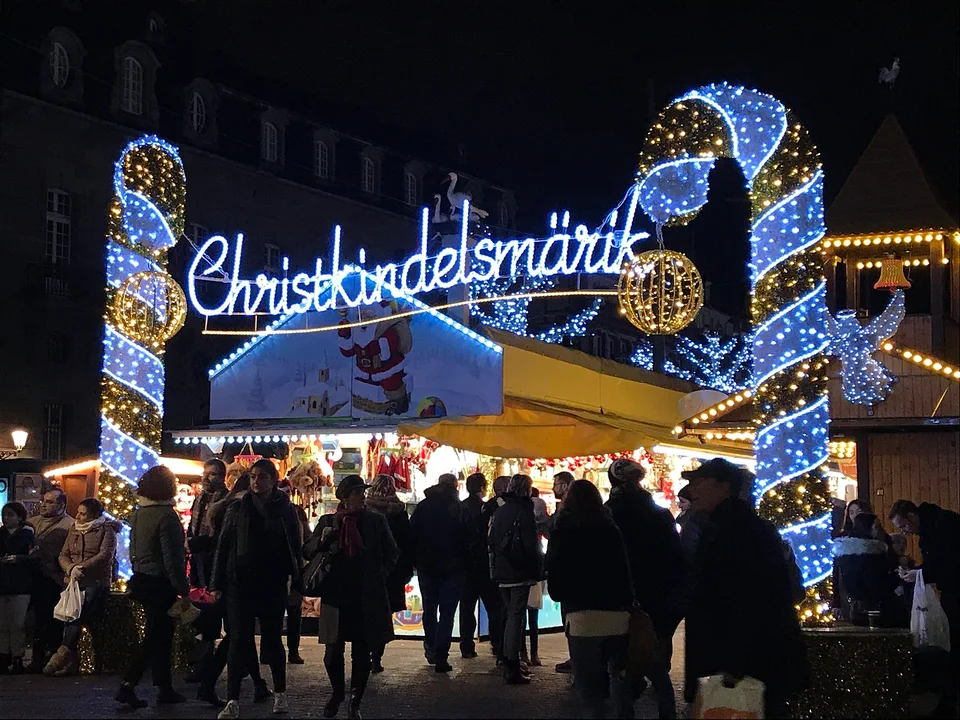 Blaue und goldene Zuckerstangen-Lichter am Eingang, Christkindelsmärik-Schriftzug und Besucher am Place Broglie in Straßburg. Archivaufnahme aus der Weihnachtszeit 2017; sie zeigt eine frühere Szene, nicht die Gestaltung von 2026.