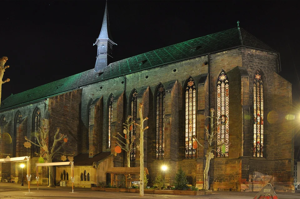 Dominikanerkirche mit beleuchteten Glasfenstern bei Nacht am Place des Dominicains in Colmar. Aufnahme des Veranstaltungsorts aus 2010 außerhalb der Weihnachtszeit; sie zeigt nicht den Markt von 2026.