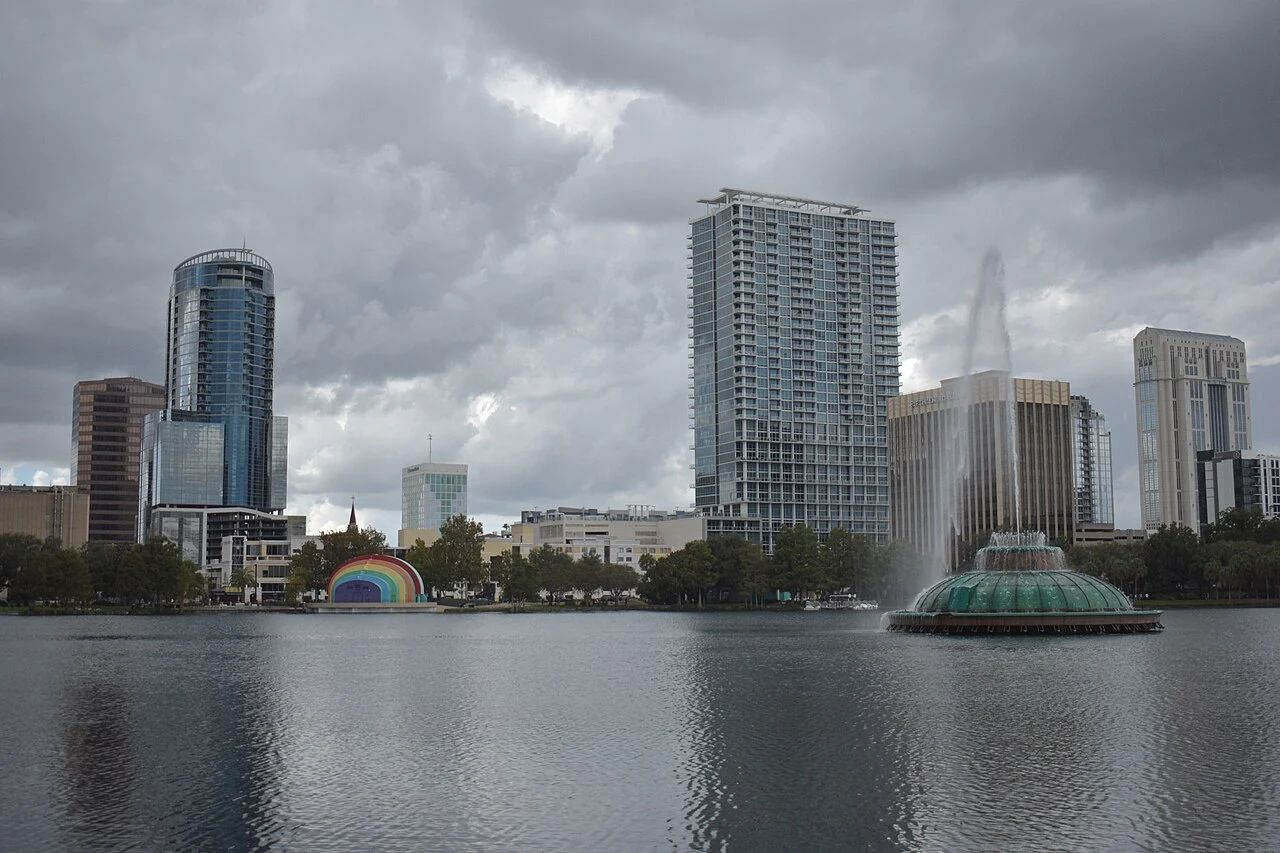 Lake Eola fountain, lakeside amphitheater and downtown Orlando skyline beneath clouds. City-context photograph taken in October 2024. It does not show a theme park or a Christmas event.