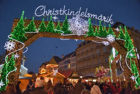 KI-generierte repräsentative Illustration. Fotovorlage: Beleuchtetes Eingangstor des Christkindelsmärik über Ständen und Besuchern am Place Broglie in Straßburg. Archivaufnahme aus der Weihnachtszeit 2013; sie zeigt eine frühere Szene, nicht die Gestaltung von 2026.