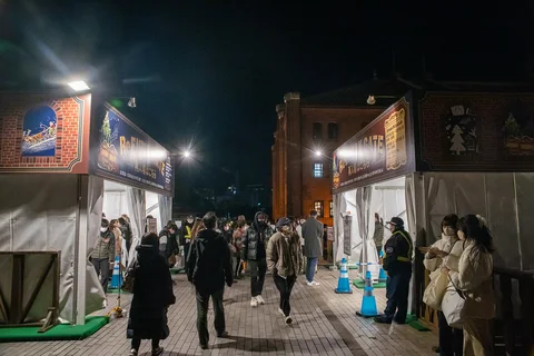 Besucher zwischen den Eingangszelten des Weihnachtsmarkts bei den Roten Backsteinlagerhäusern in Yokohama. Archivfoto von 2022; zu sehen ist eine frühere Gestaltung.