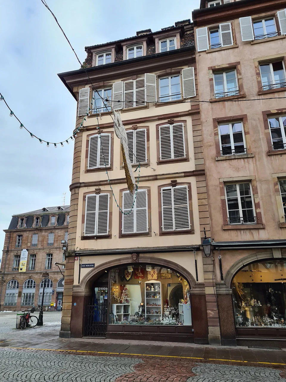 Fassade mit Fensterläden und Schaufenstern an der Rue Mercière 14, Ecke Place de la Cathédrale in Straßburg. Archivaufnahme des Ortes aus 2021; sie dokumentiert nicht den Weihnachtsmarkt von 2026.
