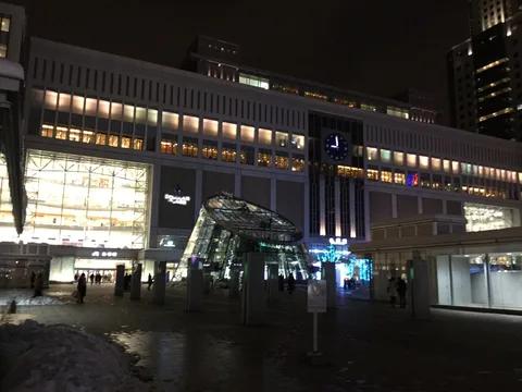 Verschneiter südlicher Vorplatz und beleuchteter Glaseingang des Bahnhofs Sapporo im Dezember 2016