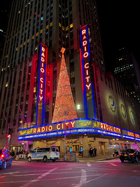 Radio City Music Hall bei Nacht mit roten Leuchtschildern und beleuchtetem Baum an der Fassade. Aufnahme vom November 2021; die angezeigten Termine gelten nicht für 2026.